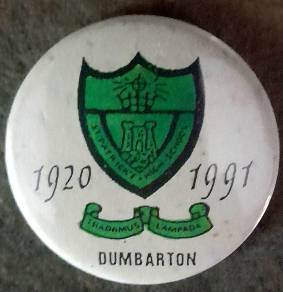 Image of a button badge from St Patrick's High School, Dumbarton. (Green shield and motto on white background. Dates showing, 1920 - 1991.